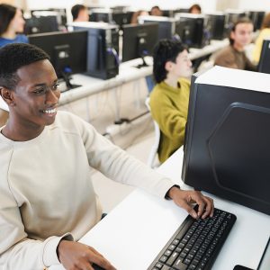 Young african student using computer inside computer room at school - Focus on left eye